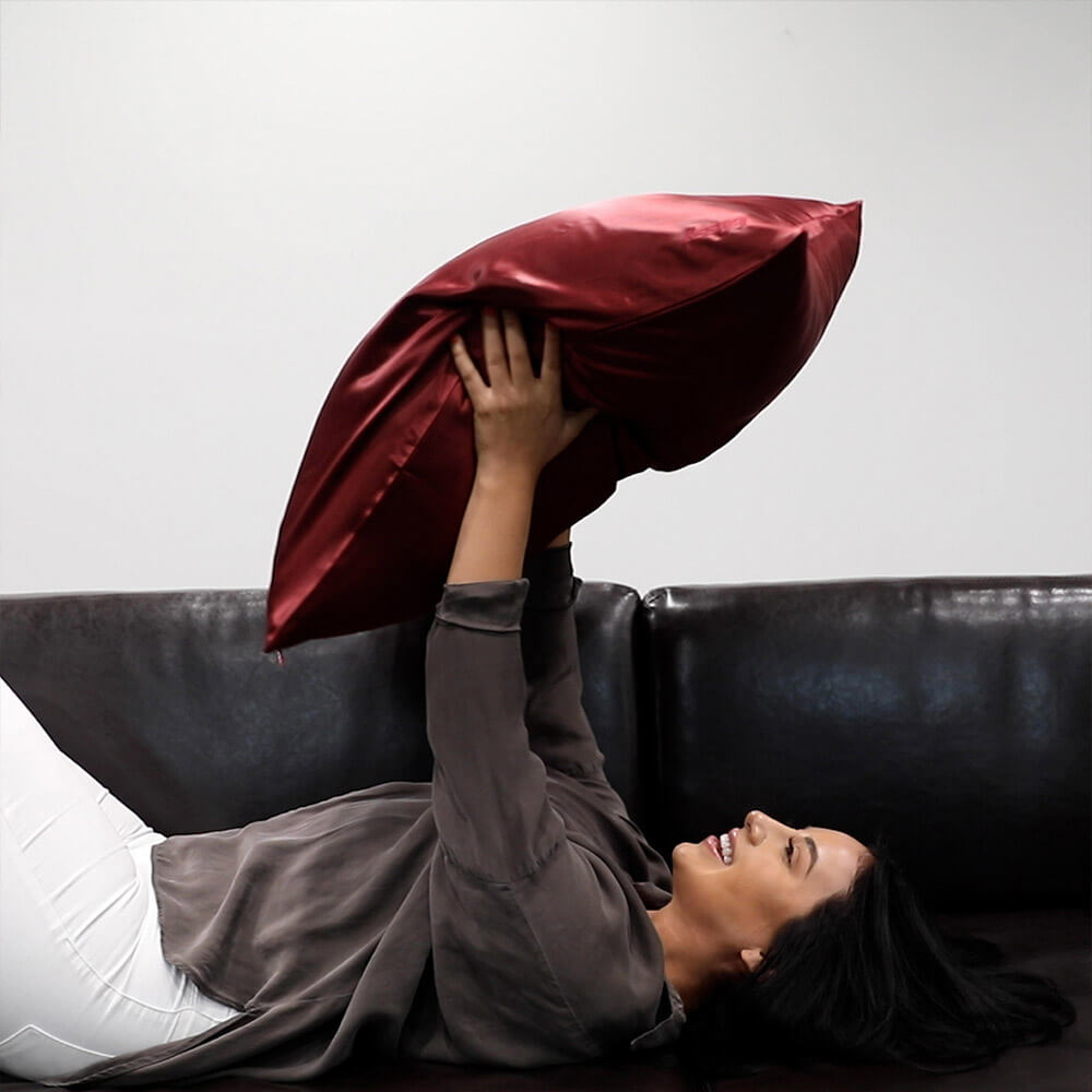 Woman holding up a burgundy Blissy silk pillowcase
